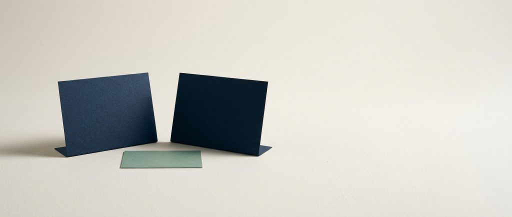 Two navy cards standing facing each other with a sage card between them, representing a question and an answer.