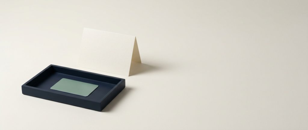 Hospitality digital management for branded and independent hotels A navy tray holding a sage key card with a folded card standing behind it, reduced to a front desk in two objects.