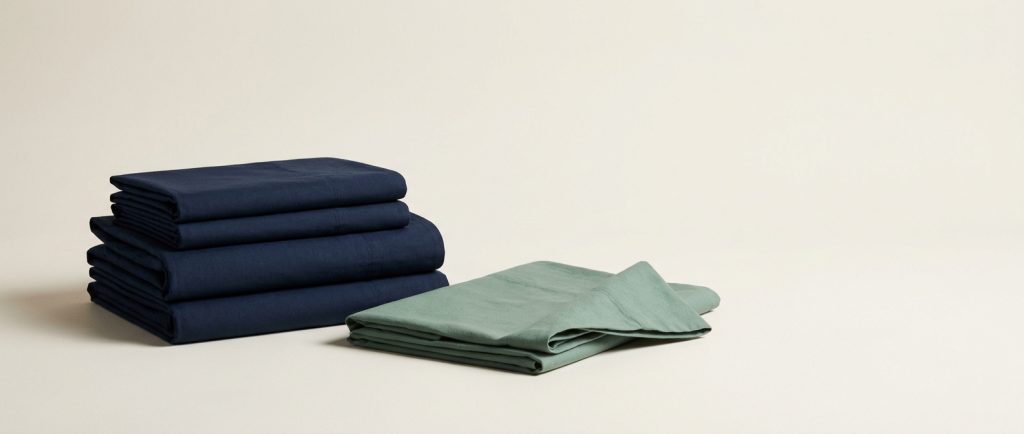 A squared stack of folded navy sheets with one sage sheet lying open beside it, representing articles published in order.