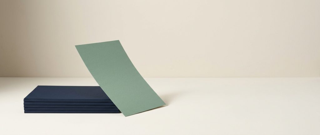 A stack of identical navy sheets with one sage sheet lifted clear, representing a backup that can actually be restored.